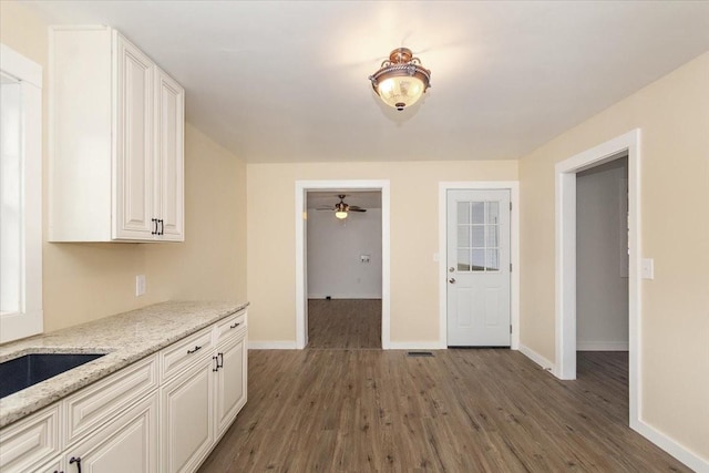 kitchen with dark wood-type flooring, white cabinets, sink, ceiling fan, and light stone counters