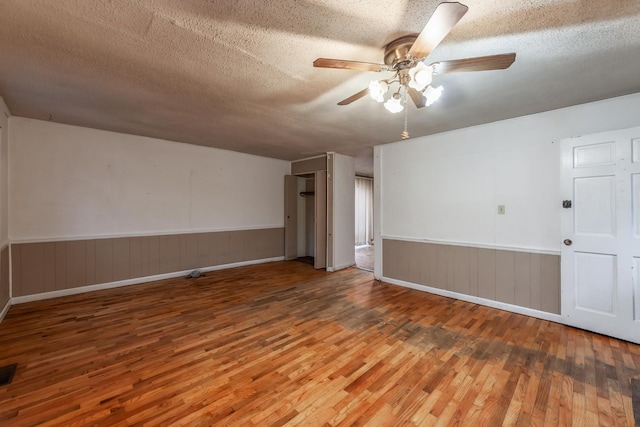 empty room with ceiling fan, wood-type flooring, and a textured ceiling