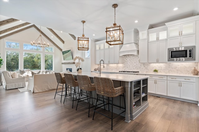 kitchen with stainless steel appliances, vaulted ceiling with beams, premium range hood, decorative light fixtures, and white cabinets