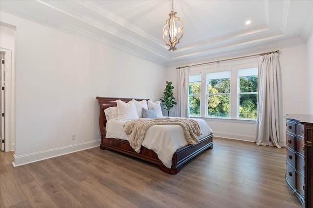 bedroom featuring a raised ceiling, crown molding, hardwood / wood-style floors, and an inviting chandelier