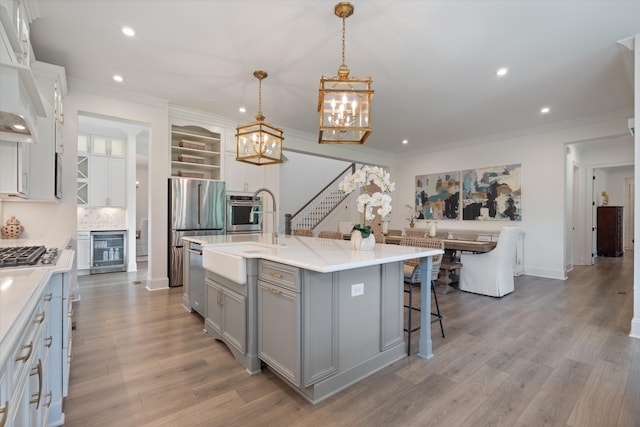 kitchen featuring pendant lighting, a kitchen island with sink, light wood-type flooring, appliances with stainless steel finishes, and beverage cooler