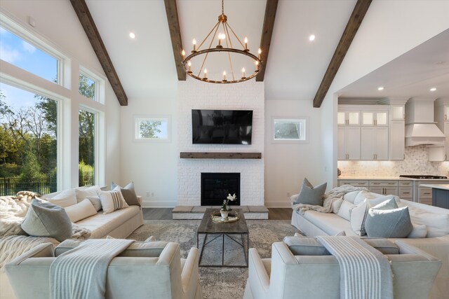 living room with vaulted ceiling with beams, light hardwood / wood-style floors, a brick fireplace, and an inviting chandelier