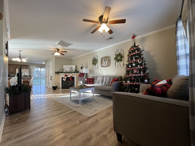 living room with a textured ceiling, ceiling fan with notable chandelier, wood-type flooring, and ornamental molding