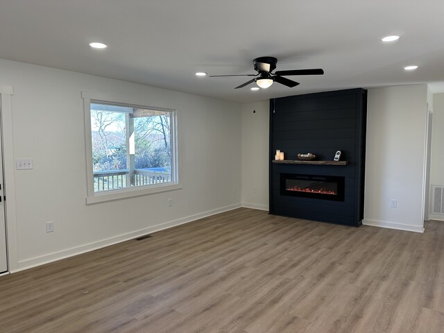 unfurnished living room with a large fireplace, light hardwood / wood-style floors, and ceiling fan