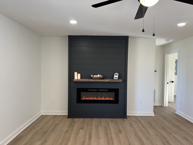 unfurnished living room with hardwood / wood-style floors, ceiling fan, and a large fireplace