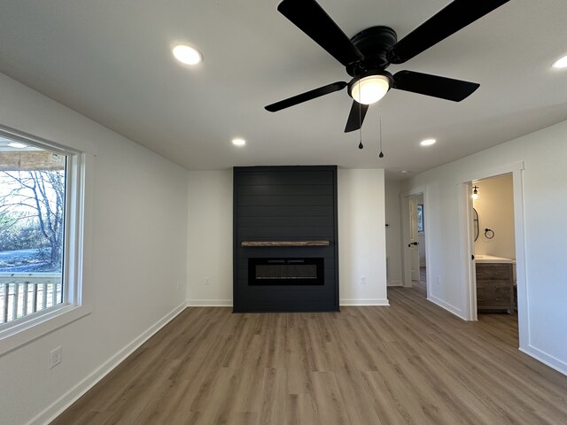 unfurnished living room featuring ceiling fan, a large fireplace, and light wood-type flooring