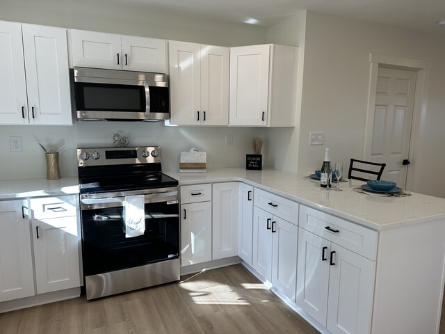 kitchen featuring white cabinets, light stone countertops, light hardwood / wood-style floors, kitchen peninsula, and stainless steel appliances