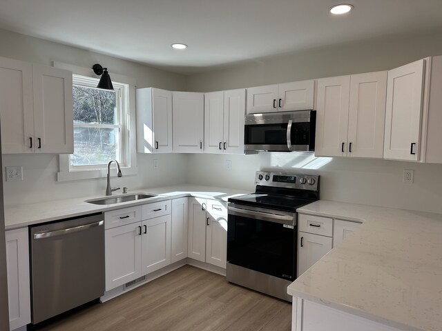 kitchen with white cabinetry, sink, stainless steel appliances, and light hardwood / wood-style floors