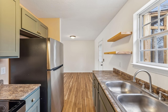 kitchen featuring sink, stainless steel fridge, light hardwood / wood-style floors, a textured ceiling, and green cabinetry