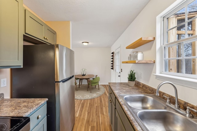 kitchen with stainless steel refrigerator, sink, green cabinets, light hardwood / wood-style floors, and a textured ceiling