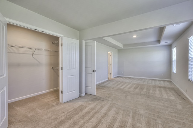 unfurnished bedroom with a closet, light carpet, and a tray ceiling