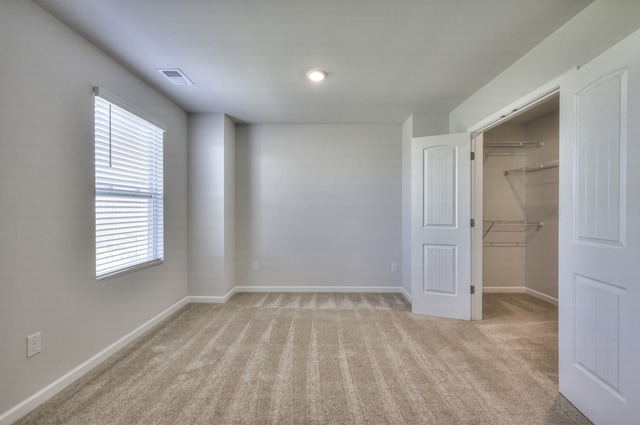 unfurnished bedroom featuring a spacious closet, light carpet, and a closet