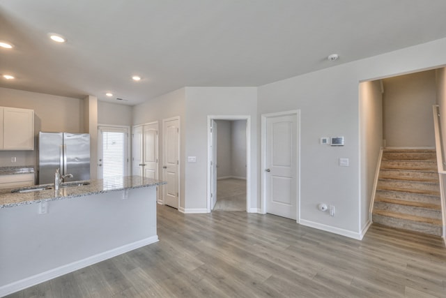 kitchen featuring sink, light hardwood / wood-style floors, light stone counters, white cabinetry, and stainless steel refrigerator