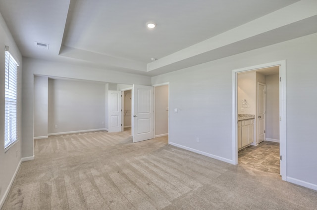 unfurnished bedroom with ensuite bathroom, a raised ceiling, and light carpet