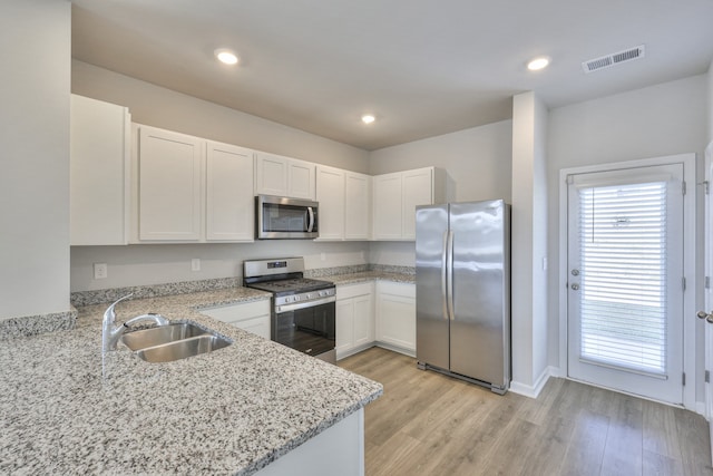 kitchen with sink, light stone counters, light hardwood / wood-style flooring, white cabinets, and appliances with stainless steel finishes