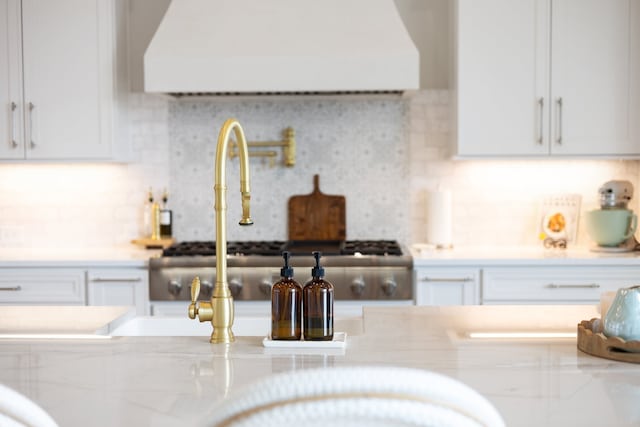 kitchen featuring white cabinetry, light stone countertops, tasteful backsplash, stainless steel range oven, and extractor fan