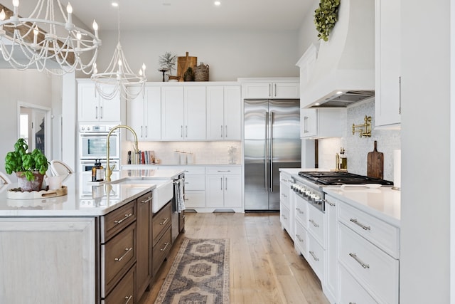 kitchen with an inviting chandelier, light wood-type flooring, custom range hood, white cabinetry, and stainless steel appliances