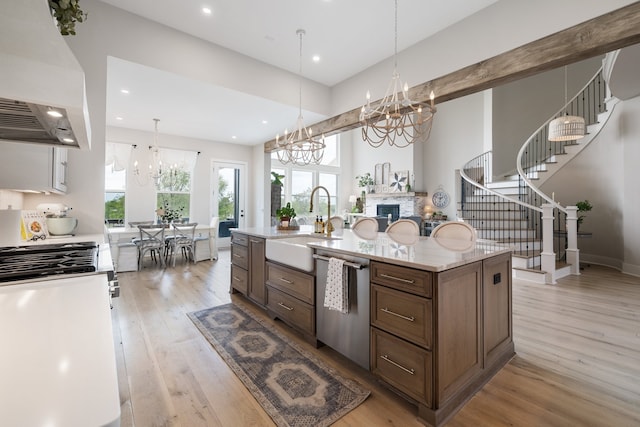 kitchen featuring light wood-type flooring, stainless steel dishwasher, extractor fan, sink, and a fireplace