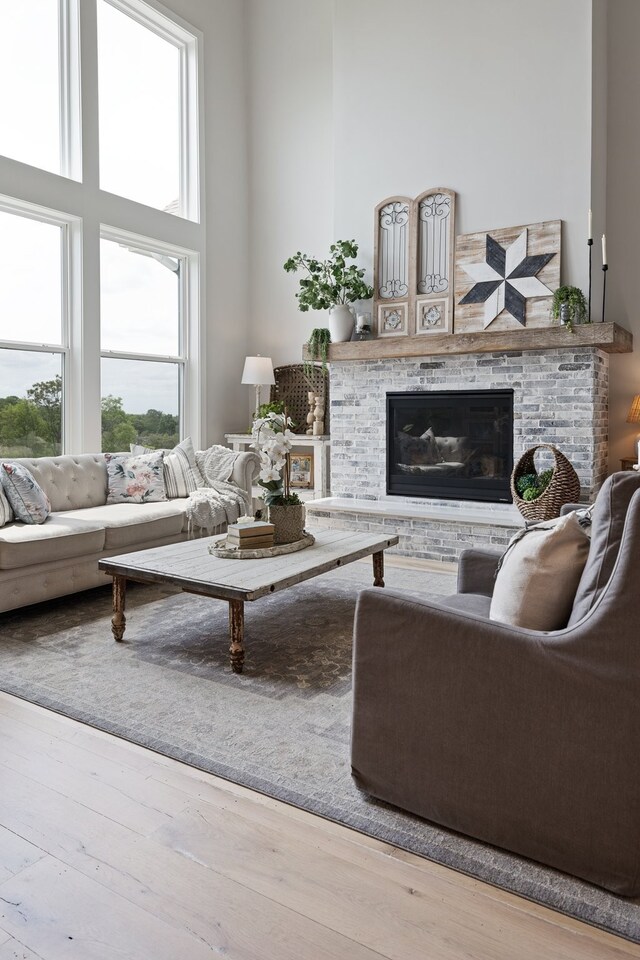 living room featuring a towering ceiling, light hardwood / wood-style flooring, and a stone fireplace