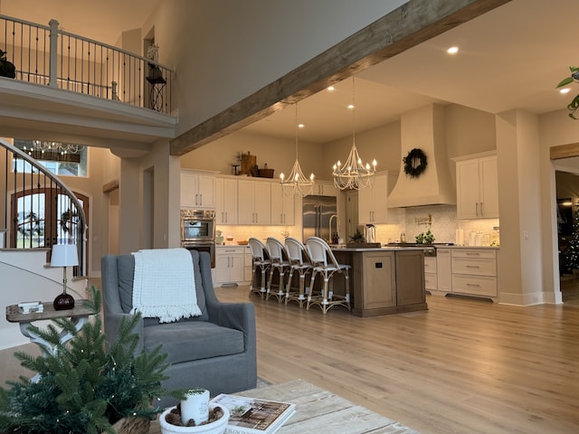 living room featuring beamed ceiling, a chandelier, a high ceiling, and light wood-type flooring