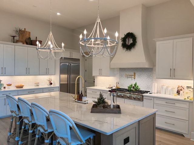 kitchen featuring a kitchen bar, appliances with stainless steel finishes, light stone counters, a spacious island, and a chandelier