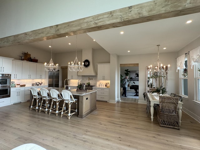 kitchen with premium range hood, a spacious island, light hardwood / wood-style flooring, decorative light fixtures, and white cabinetry