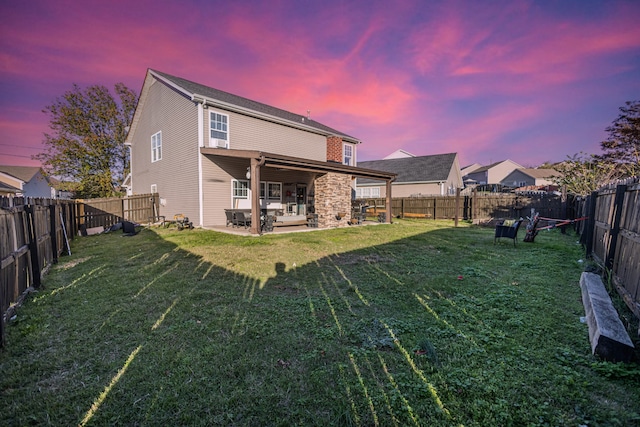 back house at dusk featuring a yard and a patio