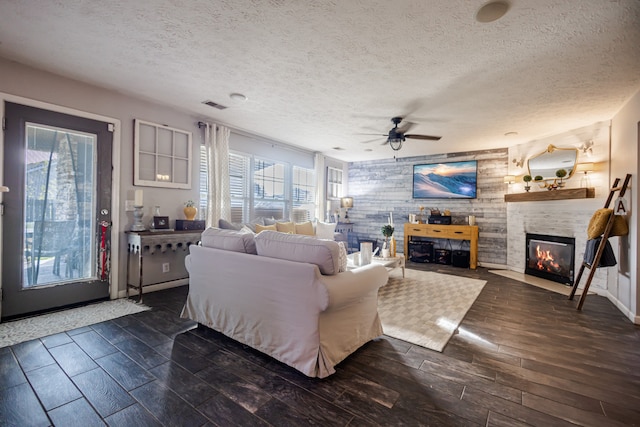 living room featuring a textured ceiling, a fireplace, ceiling fan, and dark wood-type flooring