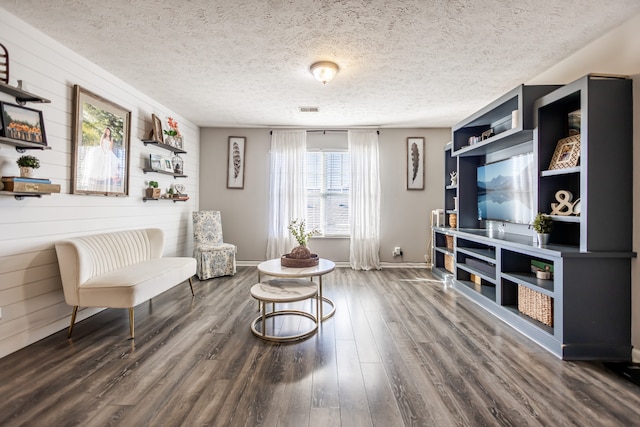 sitting room with wood walls, dark hardwood / wood-style flooring, and a textured ceiling