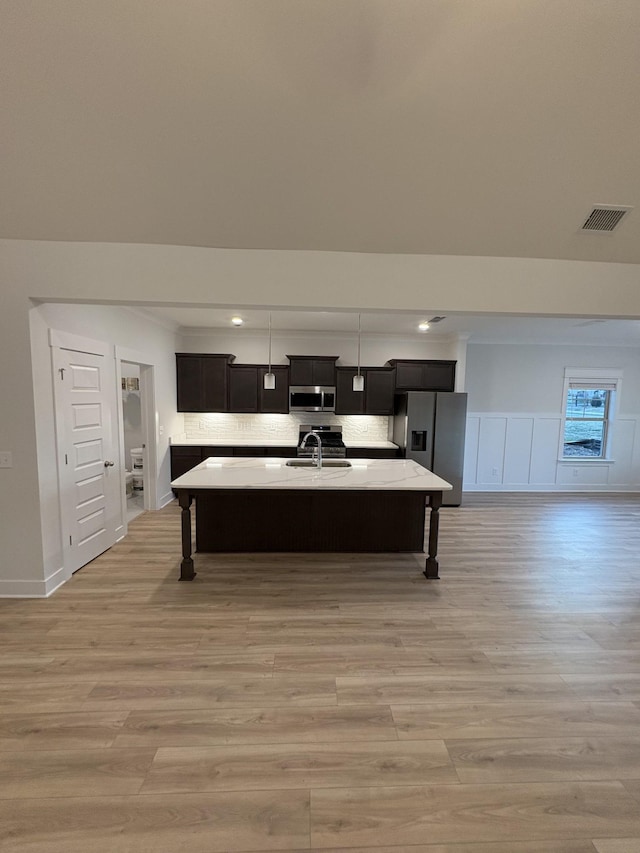 kitchen featuring sink, backsplash, a kitchen island with sink, appliances with stainless steel finishes, and light wood-type flooring