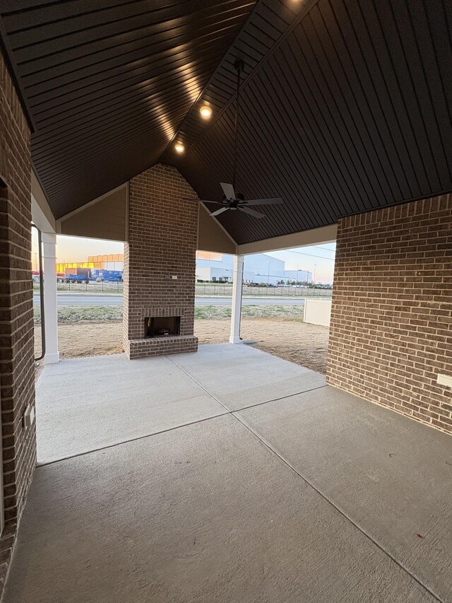 patio terrace at dusk with a water view, an outdoor brick fireplace, and ceiling fan