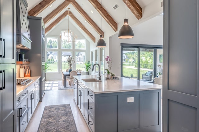 kitchen featuring sink, hanging light fixtures, an inviting chandelier, beamed ceiling, and a center island with sink