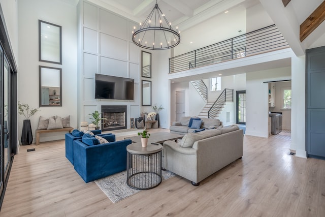 living room with a high ceiling, light wood-type flooring, an inviting chandelier, and beam ceiling