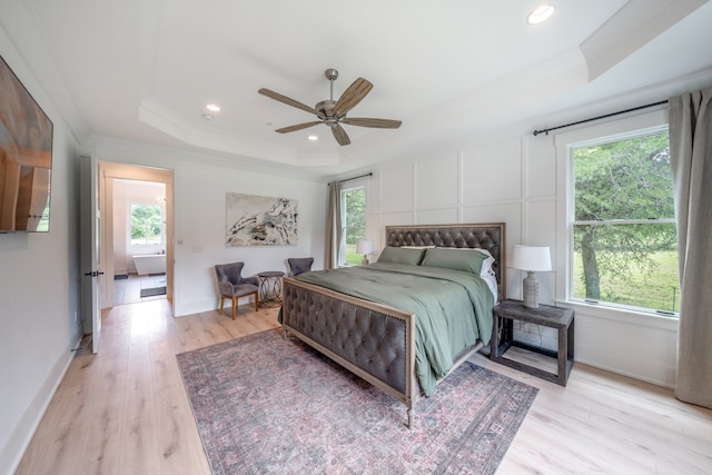 bedroom with a raised ceiling, multiple windows, ceiling fan, and light hardwood / wood-style flooring