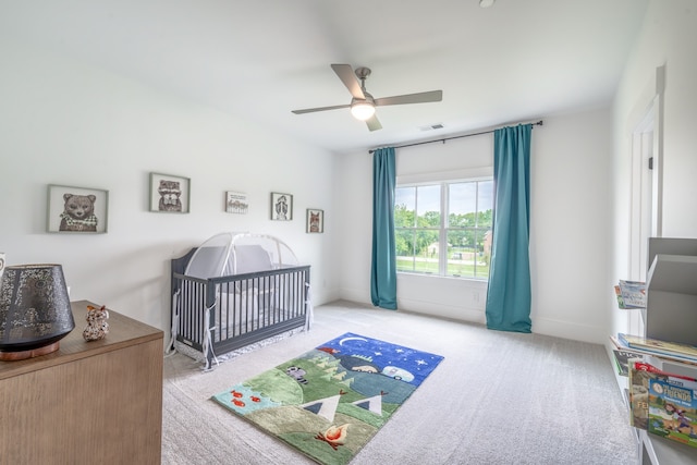 carpeted bedroom featuring a crib and ceiling fan