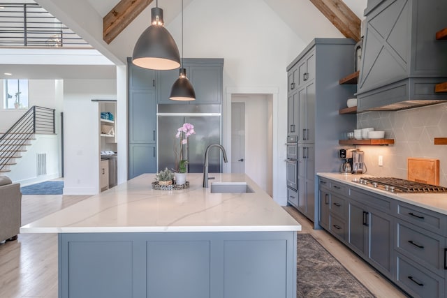 kitchen featuring beam ceiling, sink, a center island with sink, and light hardwood / wood-style flooring