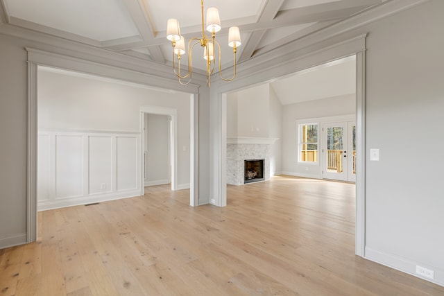 unfurnished living room featuring coffered ceiling, a stone fireplace, beam ceiling, a notable chandelier, and light hardwood / wood-style floors