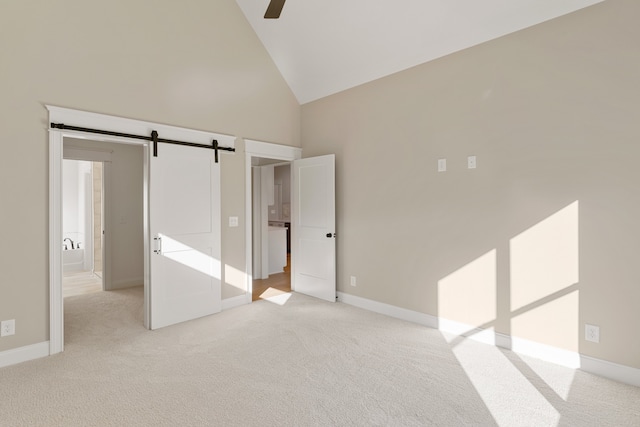 unfurnished bedroom featuring a barn door, light carpet, and high vaulted ceiling