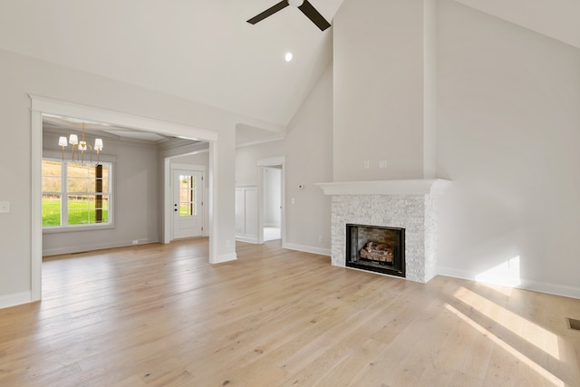 unfurnished living room with a stone fireplace, high vaulted ceiling, ceiling fan with notable chandelier, and light wood-type flooring