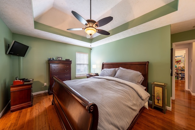 bedroom with a textured ceiling, dark hardwood / wood-style floors, ceiling fan, and a tray ceiling