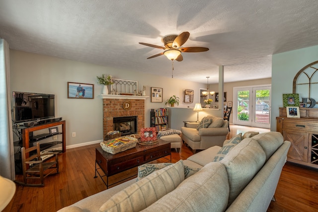 living room featuring a fireplace, ceiling fan with notable chandelier, wood-type flooring, and a textured ceiling