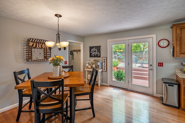 dining area featuring light hardwood / wood-style floors, a textured ceiling, and an inviting chandelier