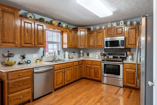 kitchen with sink, light wood-type flooring, a textured ceiling, and appliances with stainless steel finishes