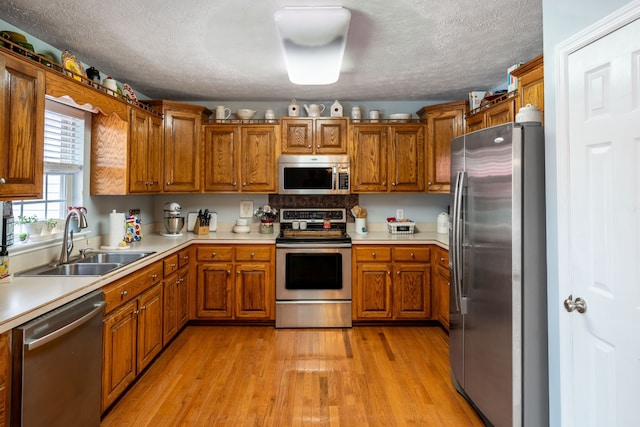 kitchen featuring sink, stainless steel appliances, a textured ceiling, and light hardwood / wood-style flooring