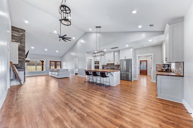 living room with light wood-type flooring, ceiling fan, and high vaulted ceiling