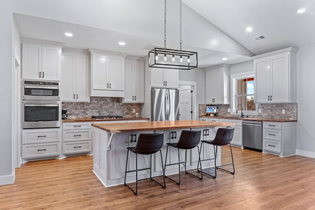 kitchen with lofted ceiling, a kitchen island, white cabinetry, appliances with stainless steel finishes, and butcher block counters