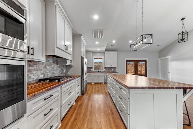 kitchen with decorative light fixtures, wooden counters, a breakfast bar area, and white cabinetry