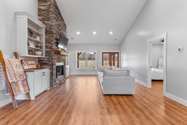 living room with ceiling fan, a high ceiling, light wood-type flooring, and a stone fireplace