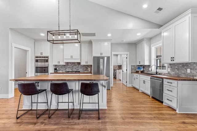 kitchen featuring stainless steel appliances, white cabinetry, wooden counters, and a kitchen island