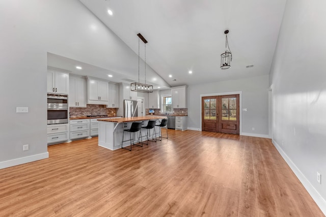 kitchen featuring wooden counters, pendant lighting, white cabinetry, stainless steel appliances, and high vaulted ceiling